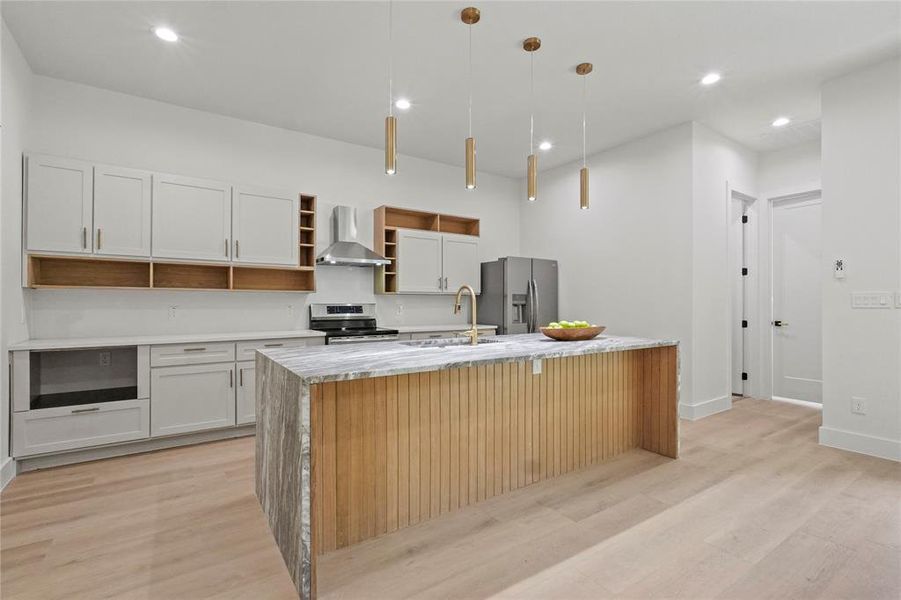 Kitchen featuring appliances with stainless steel finishes, wall chimney exhaust hood, light hardwood / wood-style flooring, and an island with sink