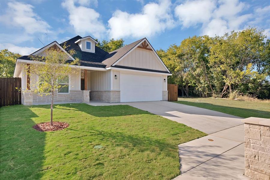 View of front of property featuring driveway, roof with shingles, stone siding, board and batten siding, and a garage