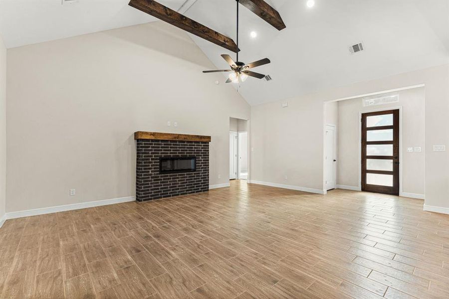 Unfurnished living room featuring a tiled fireplace, light wood-style flooring, beamed ceiling, high vaulted ceiling, and a ceiling fan