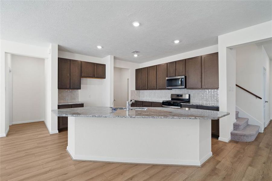 This stunning kitchen displays such a beautiful contrast with the dark stained cabinets, neutral paint, granite countertops, modern tile backsplash, SS appliances, breakfast bar, recessed lighting, high ceilings and walk in pantry.