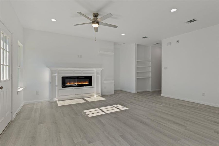 Unfurnished living room with a glass covered fireplace, ceiling fan, light wood-style floors, and recessed lighting