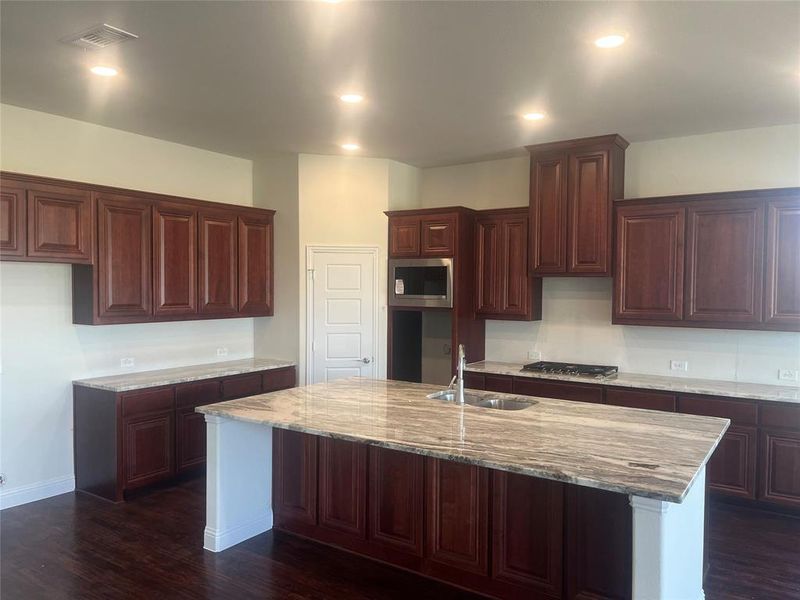 Kitchen with dark wood-type flooring, sink, appliances with stainless steel finishes, and a center island with sink