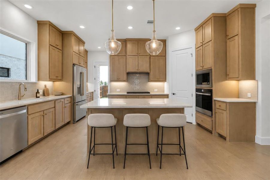 Well-appointed kitchen featuring a substantial island with seating, a stainless steel appliance suite, light wood-finish cabinetry, recessed lighting, and pendant fixtures