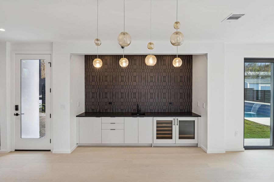 Indoor wet bar with healthy amount of natural light, white cabinets, modern cabinets, and pendant lighting