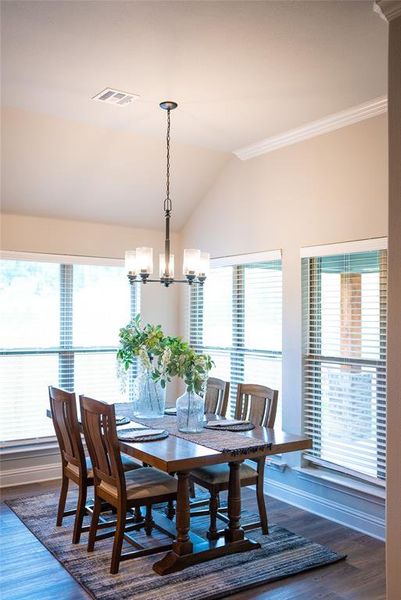 Dining room featuring wood-type flooring, lofted ceiling, ornamental molding, and an inviting chandelier