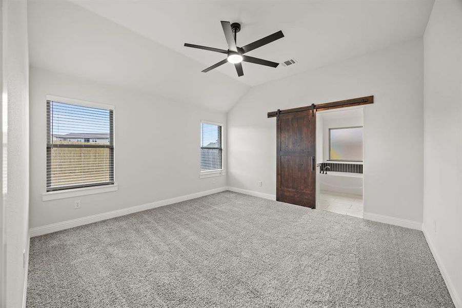 Unfurnished bedroom featuring a barn door, carpet, ceiling fan, and vaulted ceiling
