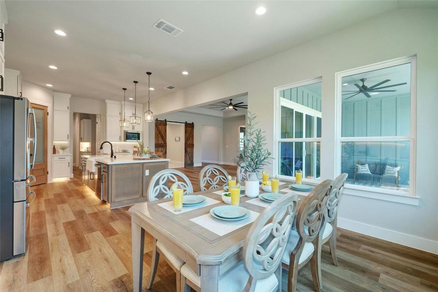 Open-concept dining area featuring wood-finish flooring, recessed lighting, and large windows overlooking an outdoor patio