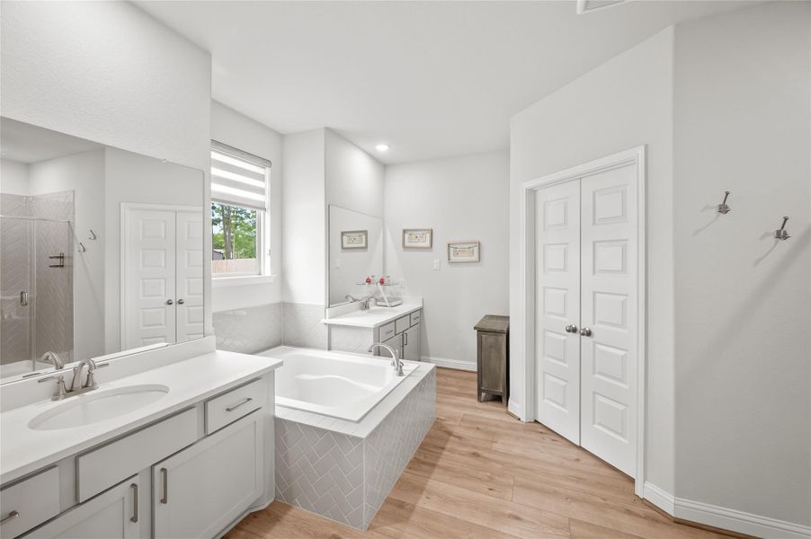 Primary bath with dual vanities, soaking tub with neutral herringbone tile, and double doors to the walk-in closet.