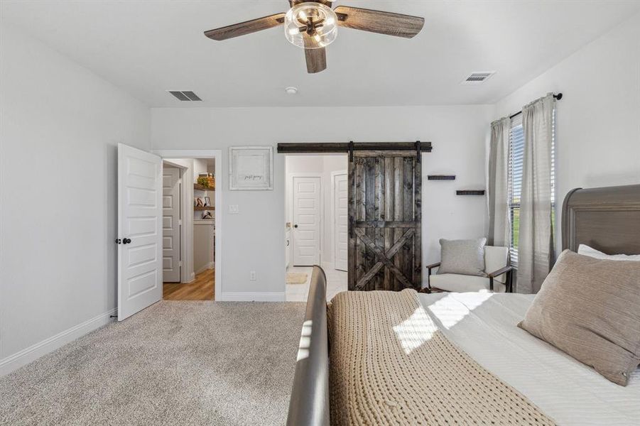 Carpeted bedroom with a barn door and ceiling fan