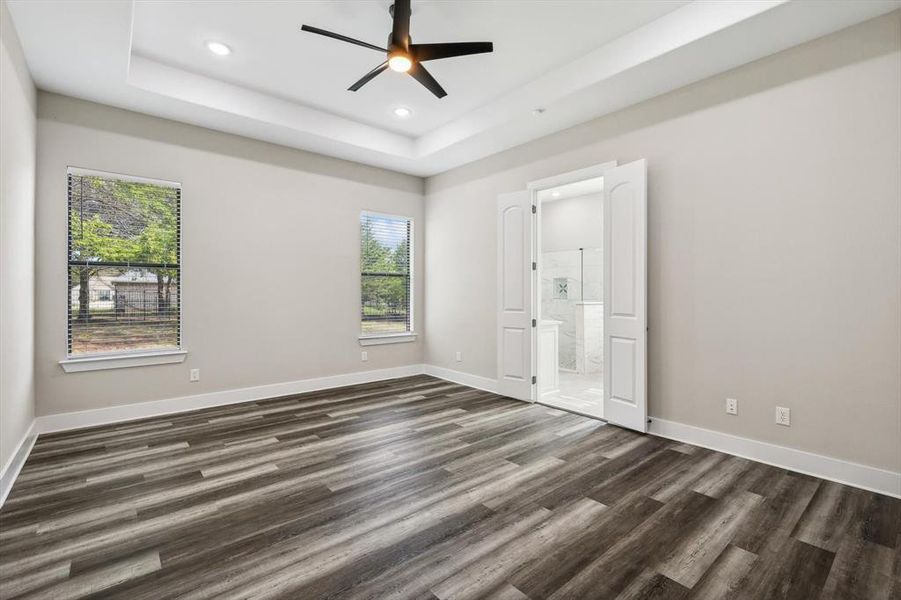 Unfurnished bedroom with ceiling fan, multiple windows, dark hardwood / wood-style floors, and ensuite bathroom