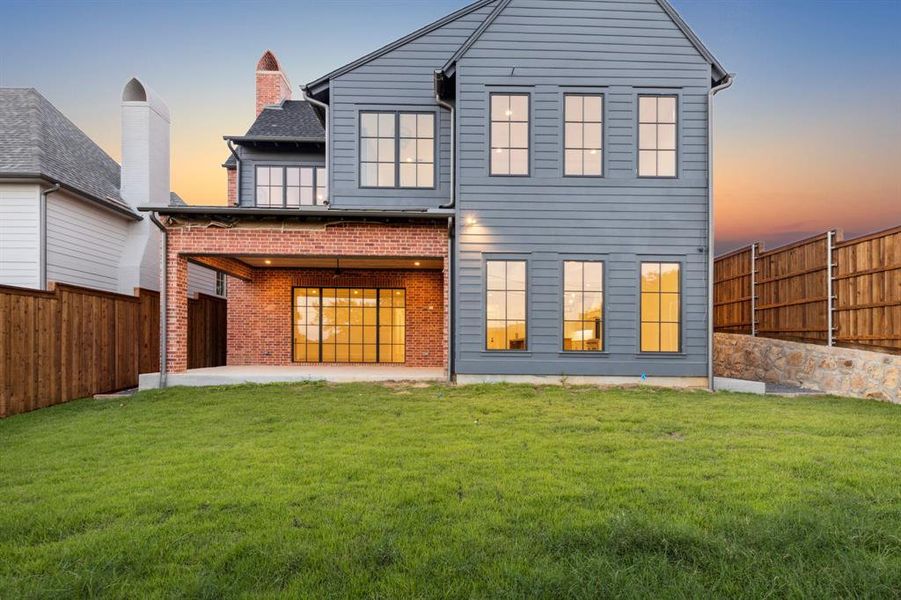 Back house at dusk featuring a lawn and a patio