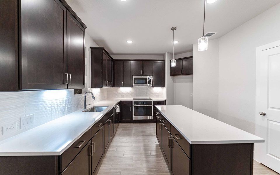 Kitchen featuring stainless steel appliances, visible vents, decorative backsplash, a sink, and dark brown cabinetry