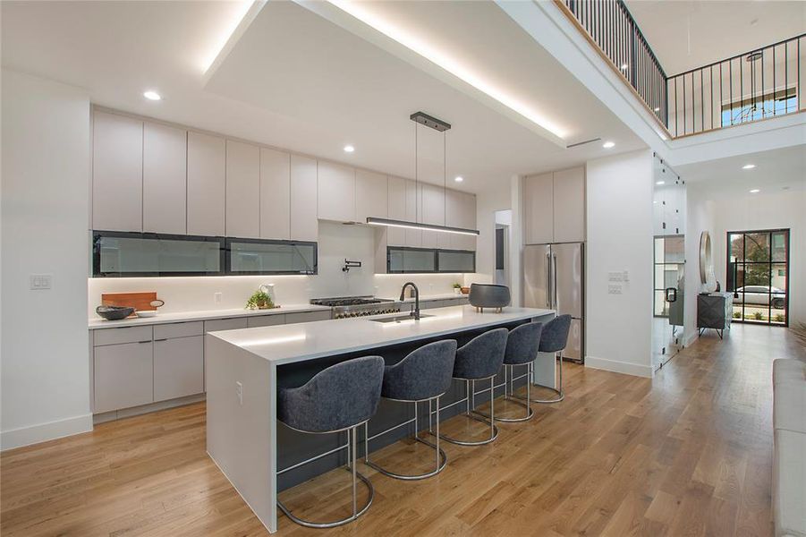 Kitchen featuring high quality fridge, a kitchen island with sink, hanging light fixtures, and light wood-type flooring