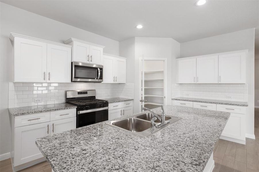 Kitchen with white cabinetry, sink, decorative backsplash, a kitchen island with sink, and stainless steel appliances