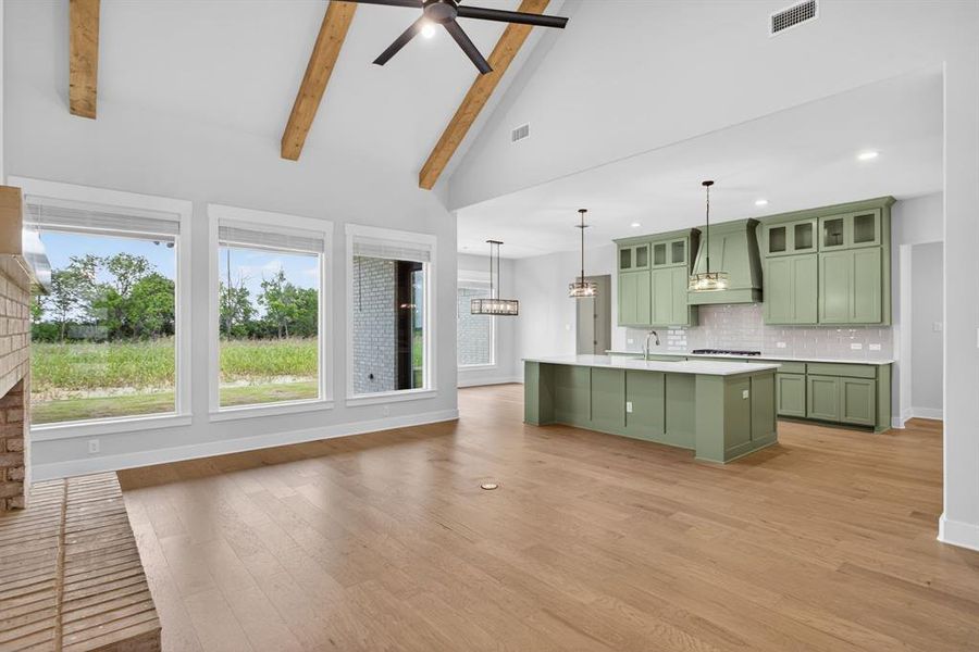 Open-concept living space featuring wood-finish flooring, a vaulted ceiling with exposed beams and a ceiling fan, and a brick-finish fireplace Open-concept living space featuring wood-finish flooring, a vaulted ceiling with exposed beams and a ceiling fan, and a brick-finish fireplace