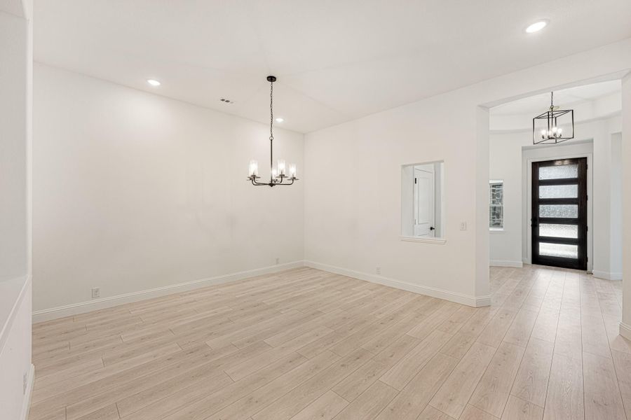 Empty dining room with light wood floors, chandelier, and view of front entry door