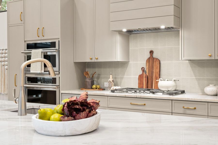Kitchen with custom range hood, decorative backsplash, light stone counters, appliances with stainless steel finishes, and gray cabinets