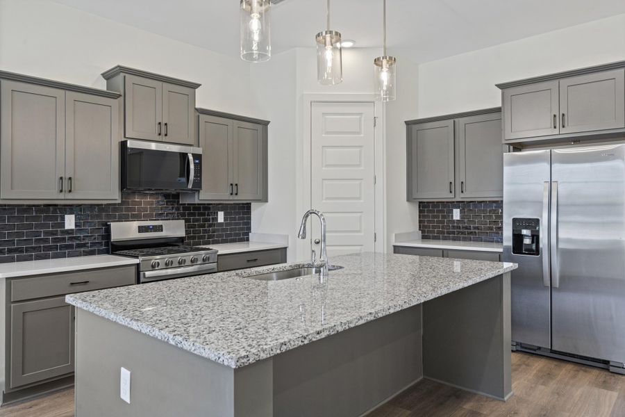 Kitchen featuring grey cabinetry, stainless steel appliances, a dark subway tile backsplash, light stone countertops, and wood-finish flooring