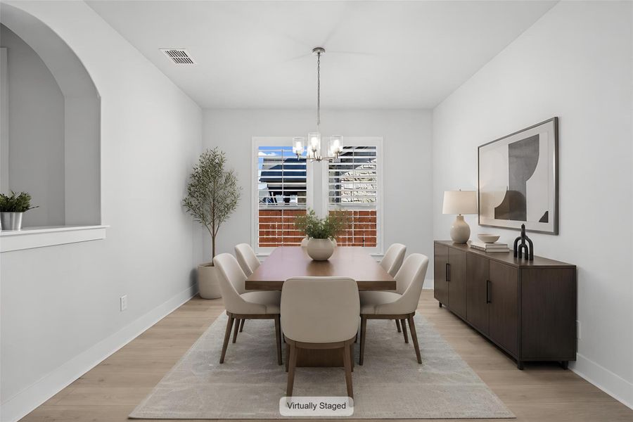 A graceful dining area, well-lit by a window, features light wood flooring and a classic chandelier.