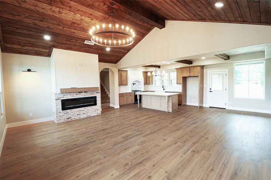 Open-concept interior featuring wood-finish flooring, a vaulted wood-paneled ceiling, and a prominent brick fireplace with an electric insert