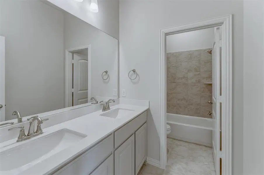 Modern bathroom with a dual vanity featuring white shaker-style cabinetry, white countertops, and brushed nickel faucets Modern bathroom with a dual vanity featuring white shaker-style cabinetry, white countertops, and brushed nickel faucets