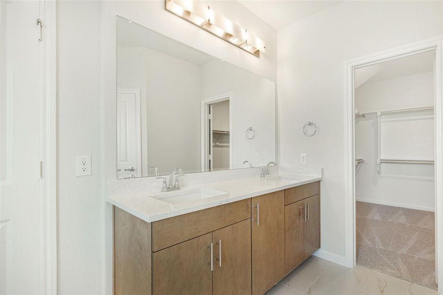 Bathroom with double sink vanity, wood cabinets, quartz countertop, and walk-in closet entrance