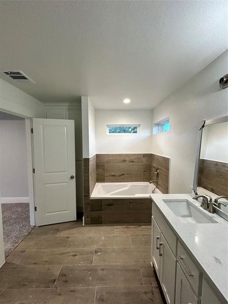 Bathroom with vanity, a textured ceiling, wood-type flooring, and tiled bath