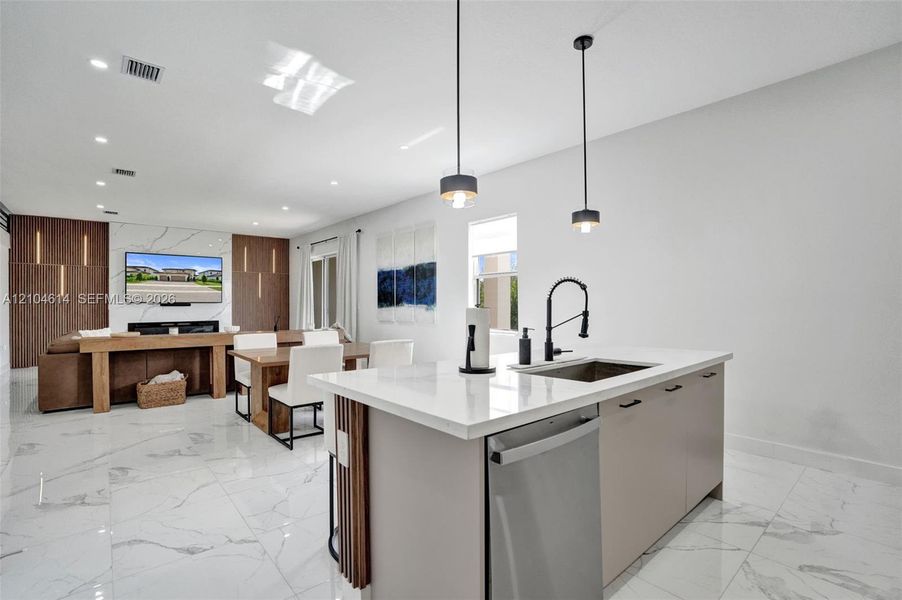 Kitchen island with a built-in sink and stainless steel dishwasher, white countertop, and pendant lighting