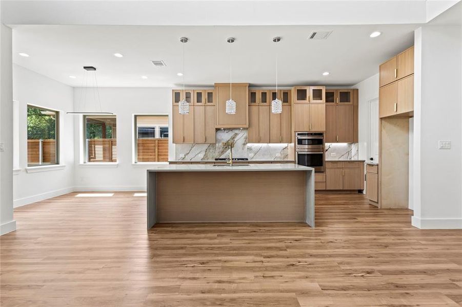 Kitchen featuring stainless steel double oven, an island with sink, light hardwood / wood-style flooring, and pendant lighting