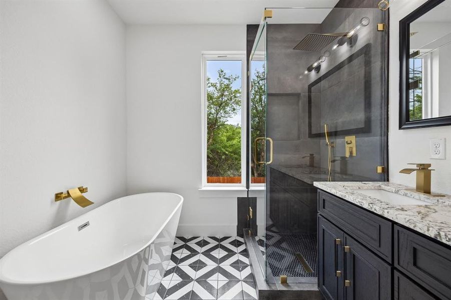 Modern bathroom featuring a freestanding soaking tub with wall-mounted brass fixture, a glass-enclosed shower with a rainfall showerhead, and a dual vanity with a stone countertop and brass faucets Modern bathroom featuring a freestanding soaking tub with wall-mounted brass fixture, a glass-enclosed shower with a rainfall showerhead, and a dual vanity with a stone countertop and brass faucets