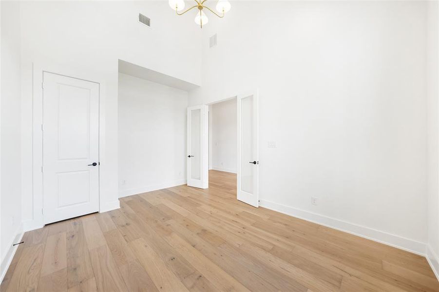 Empty room featuring a towering ceiling, a chandelier, and light wood-style floors
