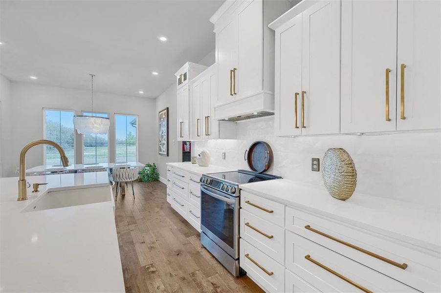 Kitchen with sink, stainless steel electric stove, white cabinets, and hanging light fixtures