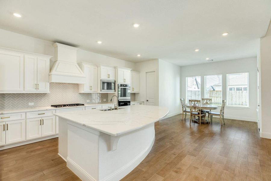This view highlights the upgraded hardware, which offers an elegant contrast against the white cabinetry. The dining area provides a picturesque overlook of the backyard, while the seamless integration of rich wood flooring and modern recessed lighting provides the perfect final touch to this sophisticated kitchen space.