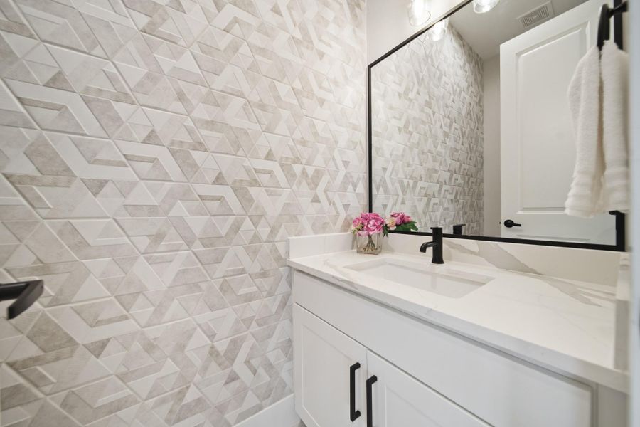 Conveniently located just off the kitchen, the half bath features a quartz countertop, sleek black faucet, and a black-framed mirror with overhead lighting. A decorative tile accent wall adds a touch of modern style to the space. Conveniently located just off the kitchen, the half bath features a quartz countertop, sleek black faucet, and a black-framed mirror with overhead lighting. A decorative tile accent wall adds a touch of modern style to the space.