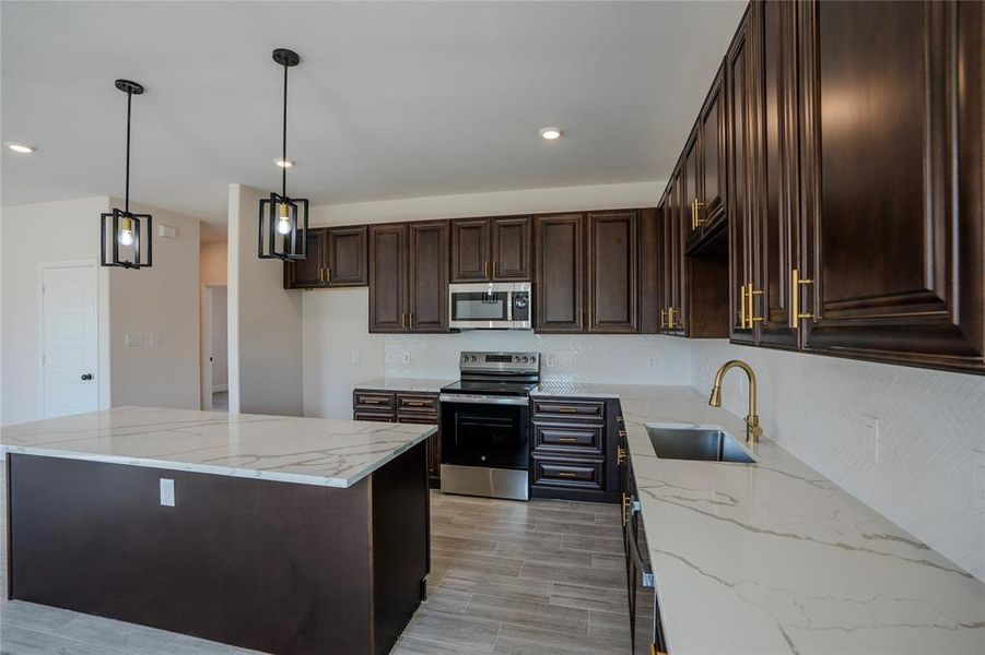 Kitchen featuring light stone counters, appliances with stainless steel finishes, pendant lighting, and sink