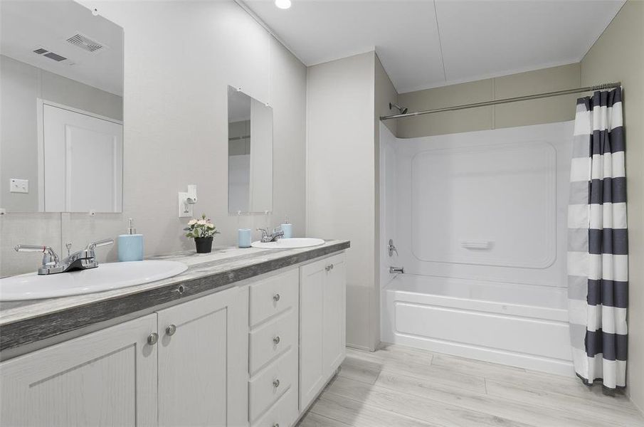 Full bath featuring shower / tub combo with curtain, double vanity, and light wood-type flooring Full bath featuring shower / tub combo with curtain, double vanity, and light wood-type flooring