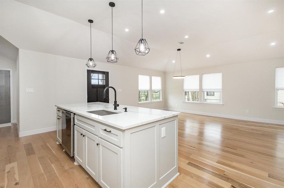 Kitchen featuring a sink, dishwasher, light wood-style flooring, white cabinetry, and a kitchen island with sink