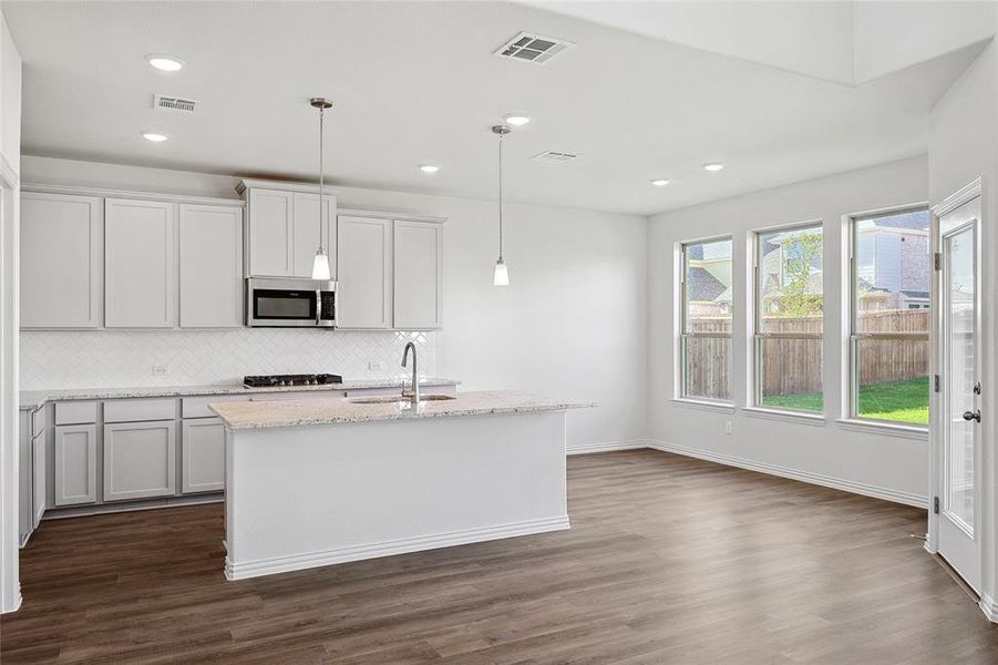 Kitchen featuring a center island with sink, tasteful backsplash, dark wood-type flooring, sink, and pendant lighting