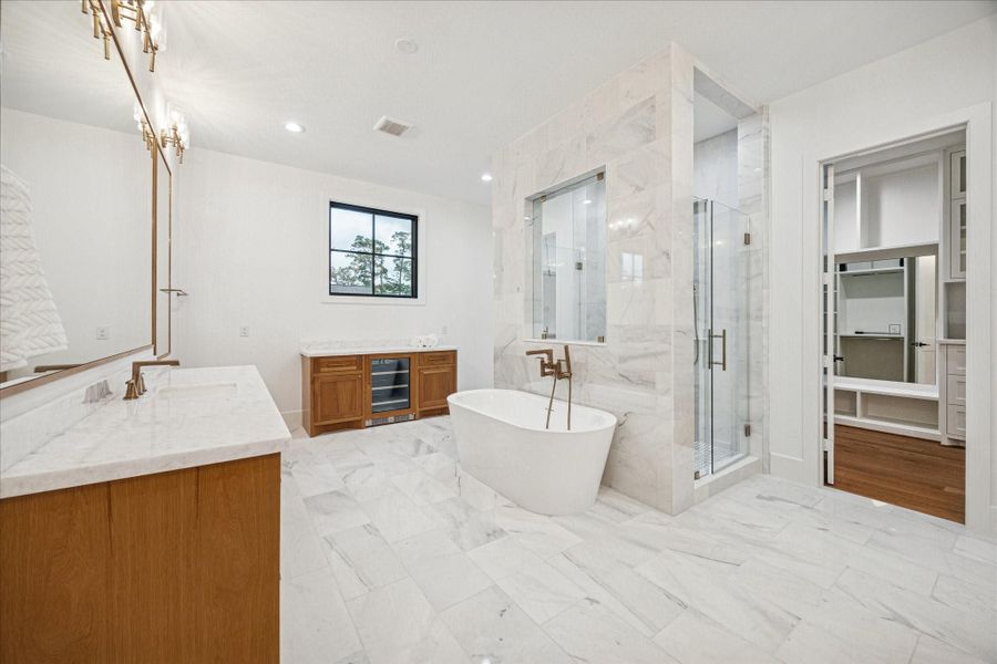 Marble walls rise around a sculptural soaking tub set against a glass-enclosed shower. Brass plumbing adds warmth, while dual vanities and custom cabinetry elevate both experience and functionality. High-efficiency windows brighten the spa-like space. *Previous Project*