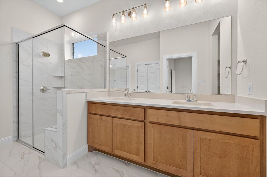 Bathroom with double vanity, light marble finish flooring, and a shower stall