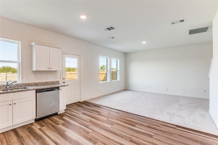 Kitchen with white cabinetry, stainless steel dishwasher, light stone countertops, recessed lighting, and light wood finished floors
