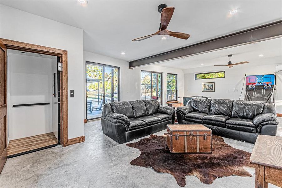 Living area with concrete flooring, beam ceiling, ceiling fan, elevator, and recessed lighting