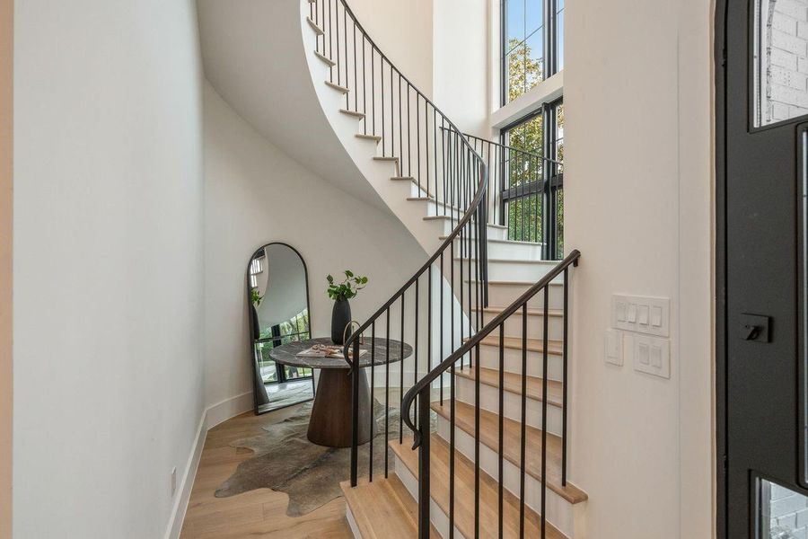 Two-story foyer with a dramatic curved staircase, floor-to-ceiling windows and designer iron railing.
