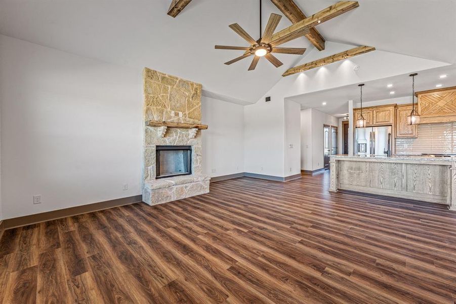 Unfurnished living room featuring beamed ceiling, dark wood-type flooring, a ceiling fan, a fireplace, and high vaulted ceiling
