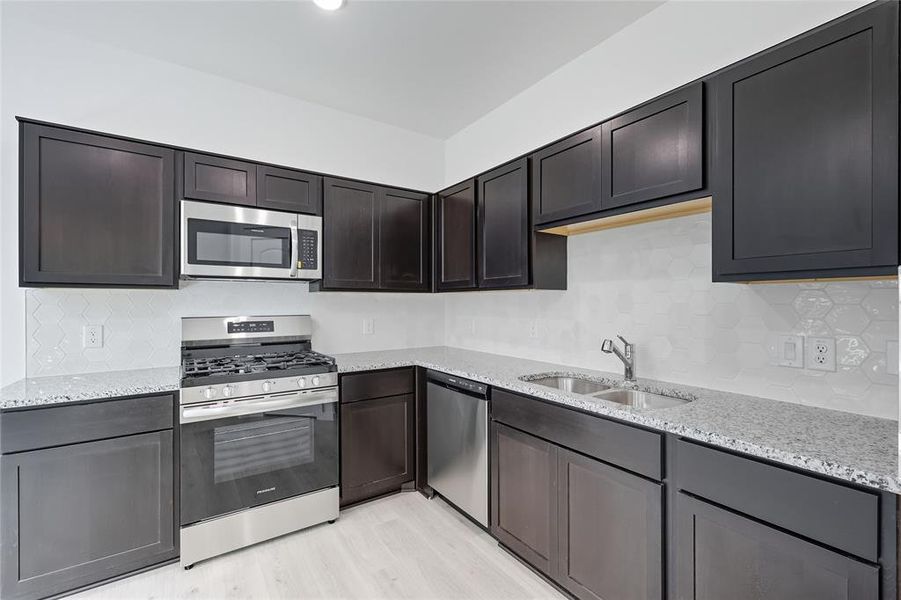 Kitchen featuring stainless steel appliances, decorative backsplash, light stone countertops, and light wood finished floors Kitchen featuring stainless steel appliances, decorative backsplash, light stone countertops, and light wood finished floors