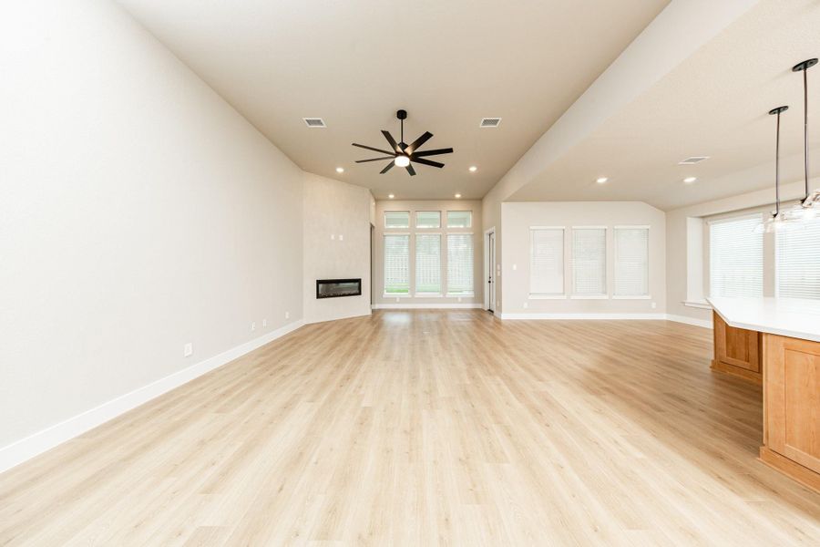 The open and airy Family Room is designed for seamless entertaining and showcasing striking architectural details with large tall windows, high ceilings with ceiling fan, recessed lighting, a beautiful electric fireplace, and durable flooring.