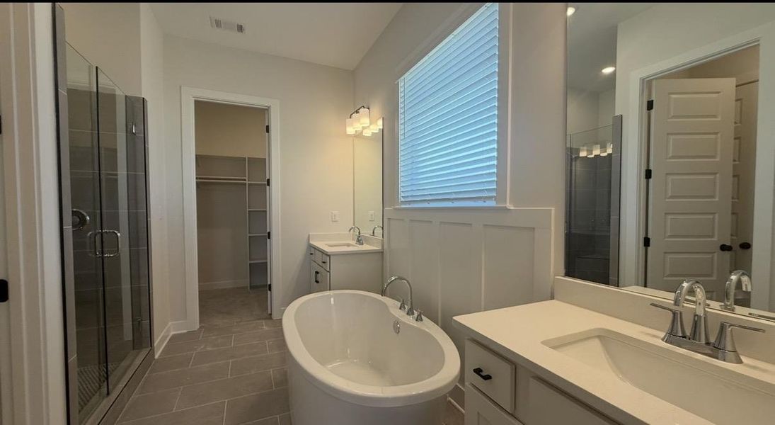 Bathroom with two vanities, a spacious closet, a stall shower, a freestanding tub, and dark tile patterned flooring