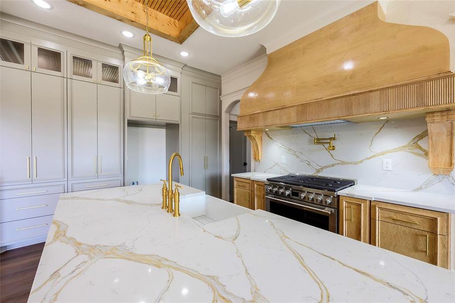 Kitchen with high end stove, glass insert cabinets, light stone countertops, decorative backsplash, and hanging light fixtures
