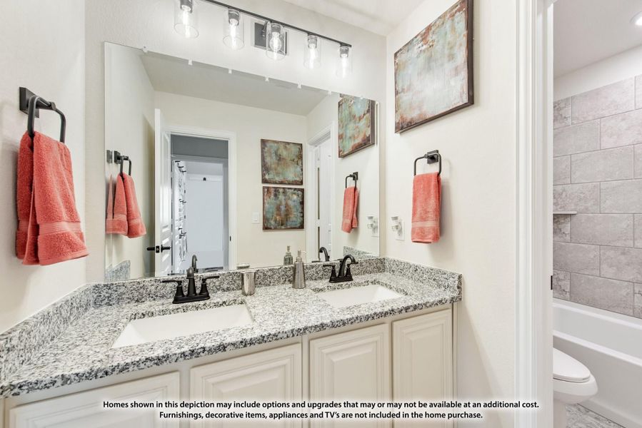 Bathroom with double sink vanity, granite countertop, large mirror, and tiled tub surround visible on the right.