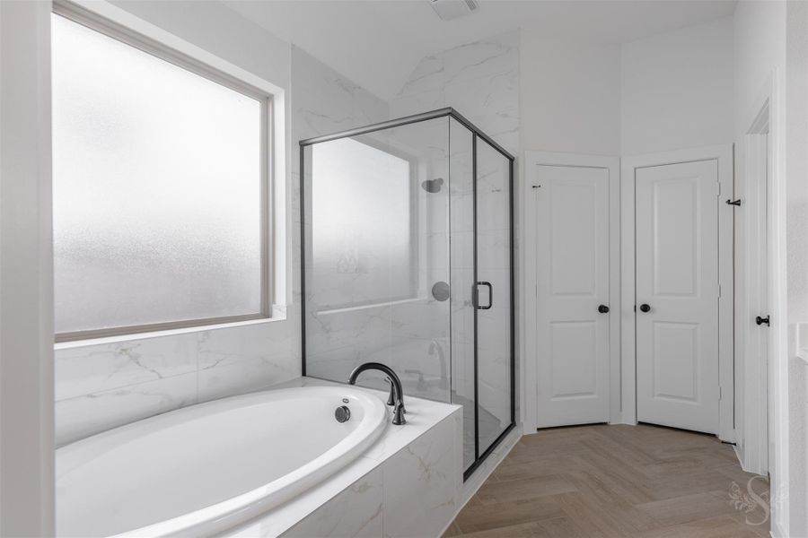 Indulge in the soaking tub surrounded by elegant marble-look tile, perfectly positioned beneath soft natural light. The adjacent glass-enclosed shower and spacious layout create a true spa-like sanctuary. Indulge in the soaking tub surrounded by elegant marble-look tile, perfectly positioned beneath soft natural light. The adjacent glass-enclosed shower and spacious layout create a true spa-like sanctuary.